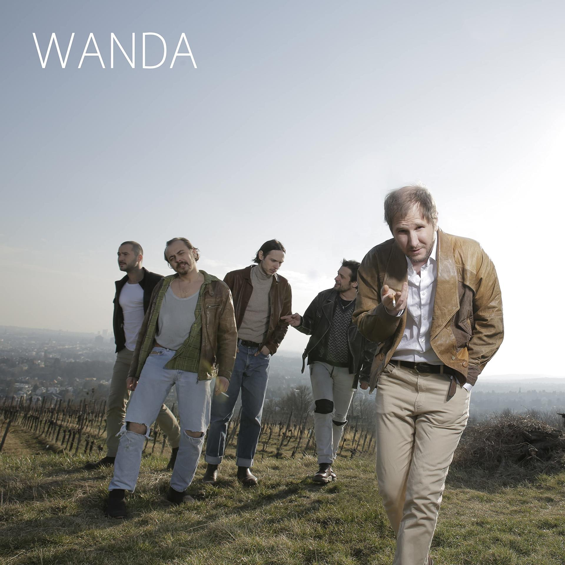 Band WANDA geht auf den Betrachter zu in einem Weinberg. Ein Mitglied raucht eine Zigarette, der Himmel ist klar.