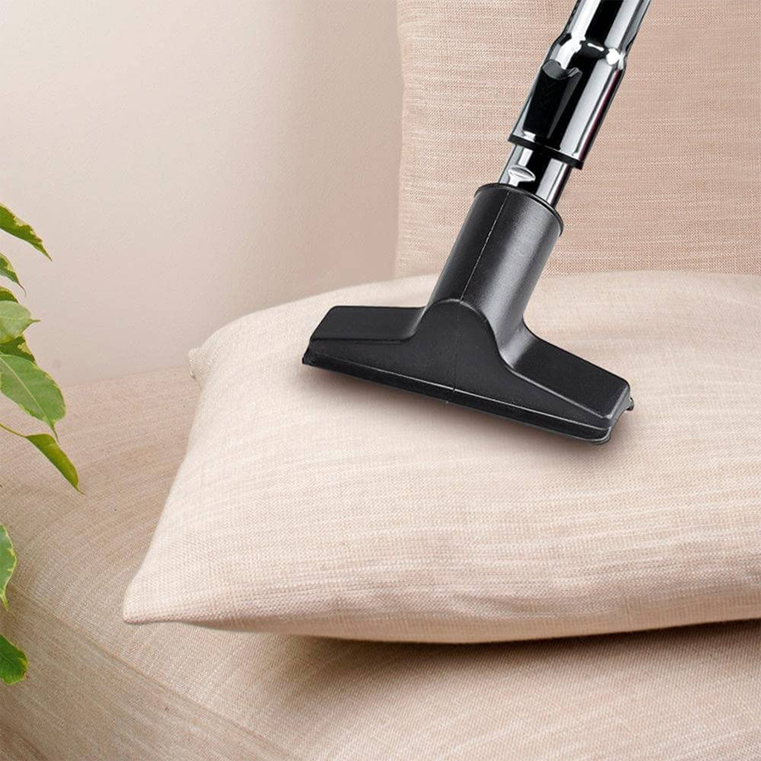 Testa dell'aspirapolvere che pulisce un cuscino beige su un divano beige, ripresa ravvicinata.