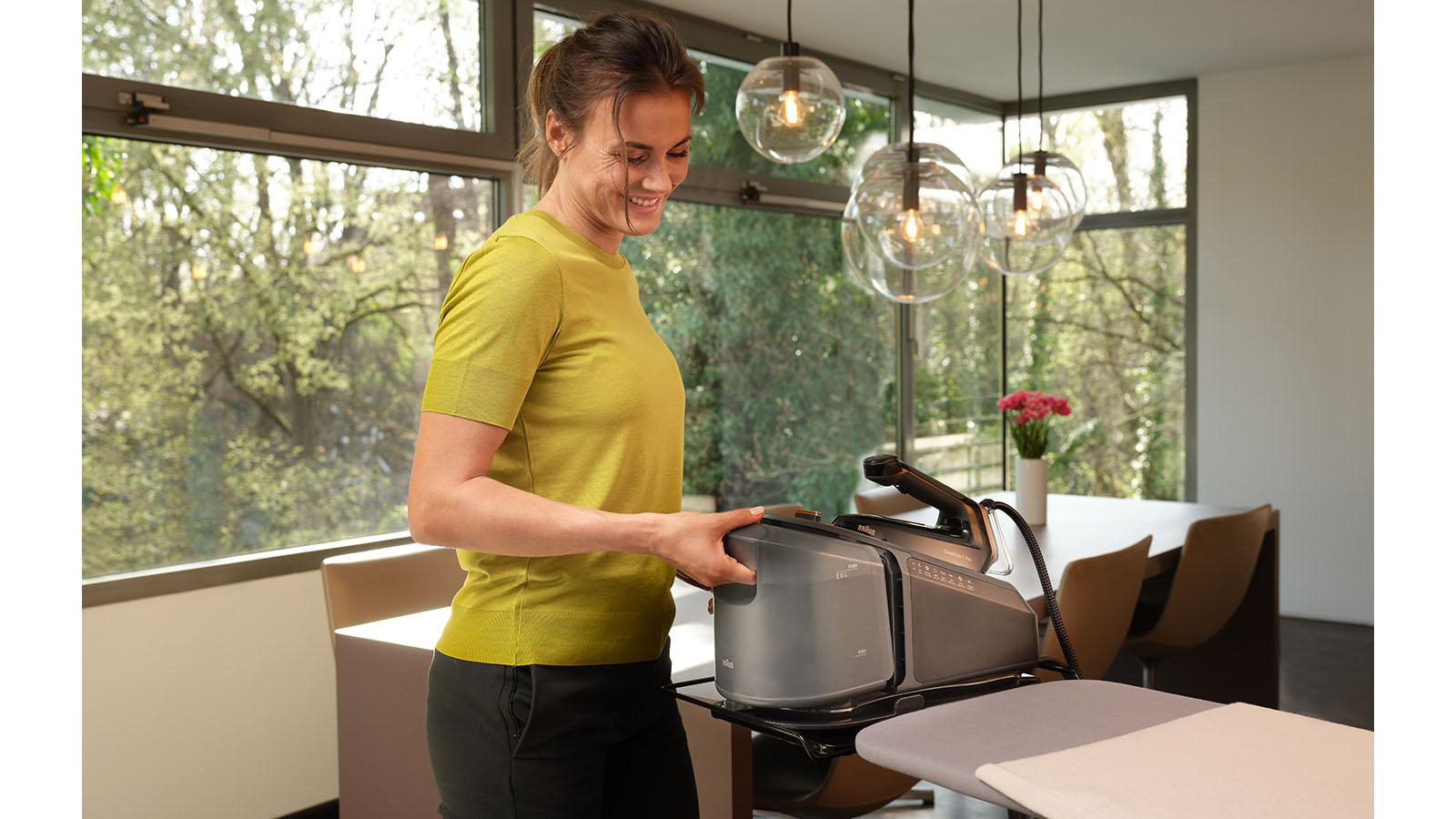 Lächelnde Frau, Bügeleisen auf Bügelbrett. Modernes Interieur mit Fenstern.