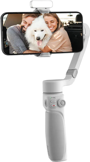 Een witte gimbal houdt een telefoon vast met een lachend stel en een hond. De gimbal heeft knoppen en een handvat.