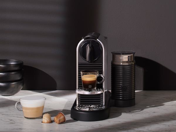 Macchina da caffè Nespresso con tazza di caffè e capsule. Macchina e montalatte neri.