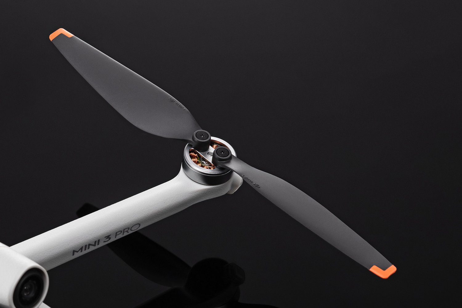 Propeller van een drone, zwarte bladen met oranje uiteinden, tegen een zwarte achtergrond.
