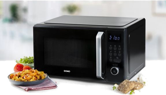 Black microwave with digital display, food on the left, and bread on the right, on a white surface.