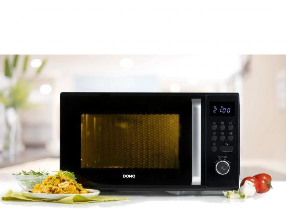 A black microwave oven with a plate of food and tomatoes on a table.
