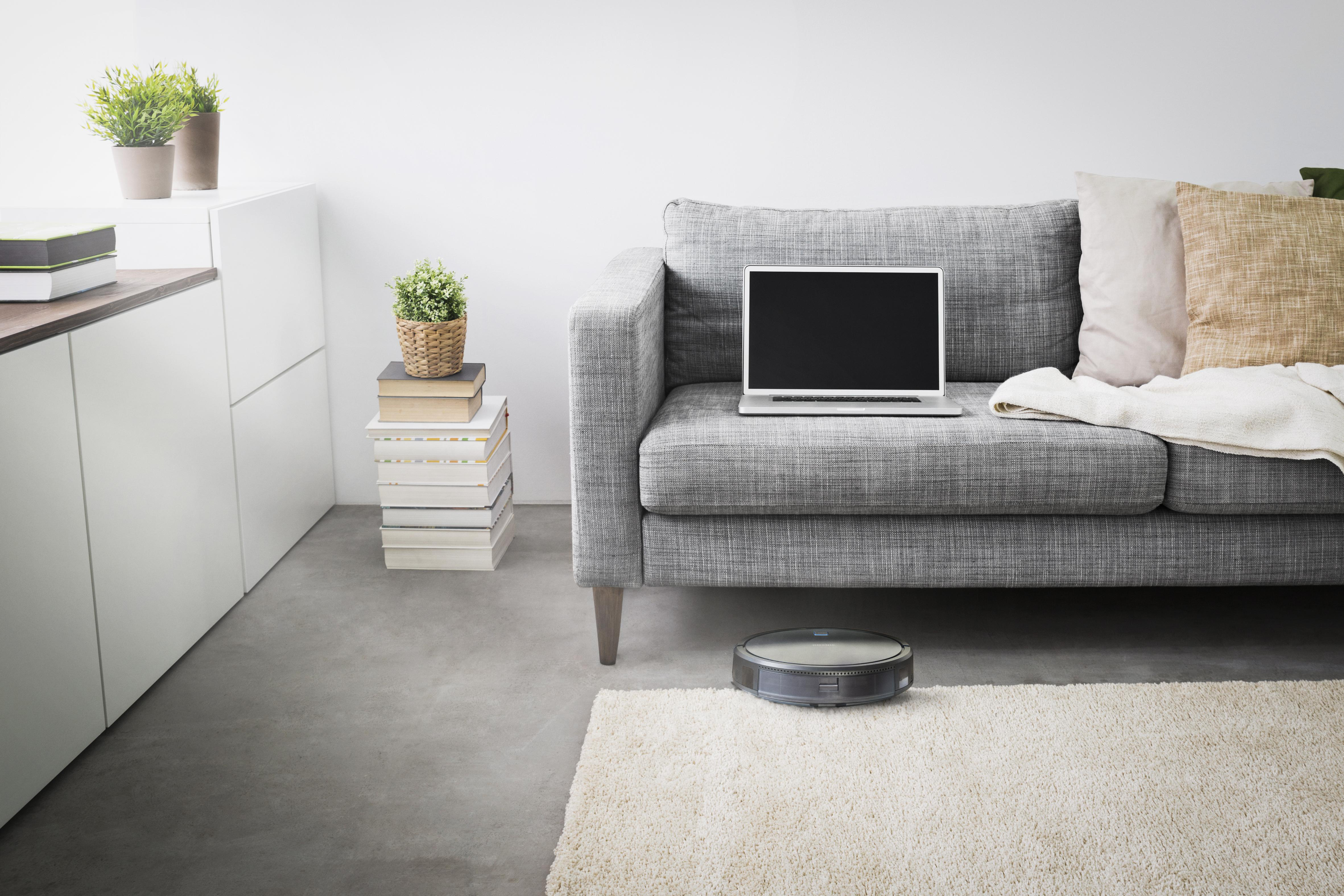 Wohnzimmer, Laptop auf Sofa, Roboter-Staubsauger, Bücher, Pflanzen.