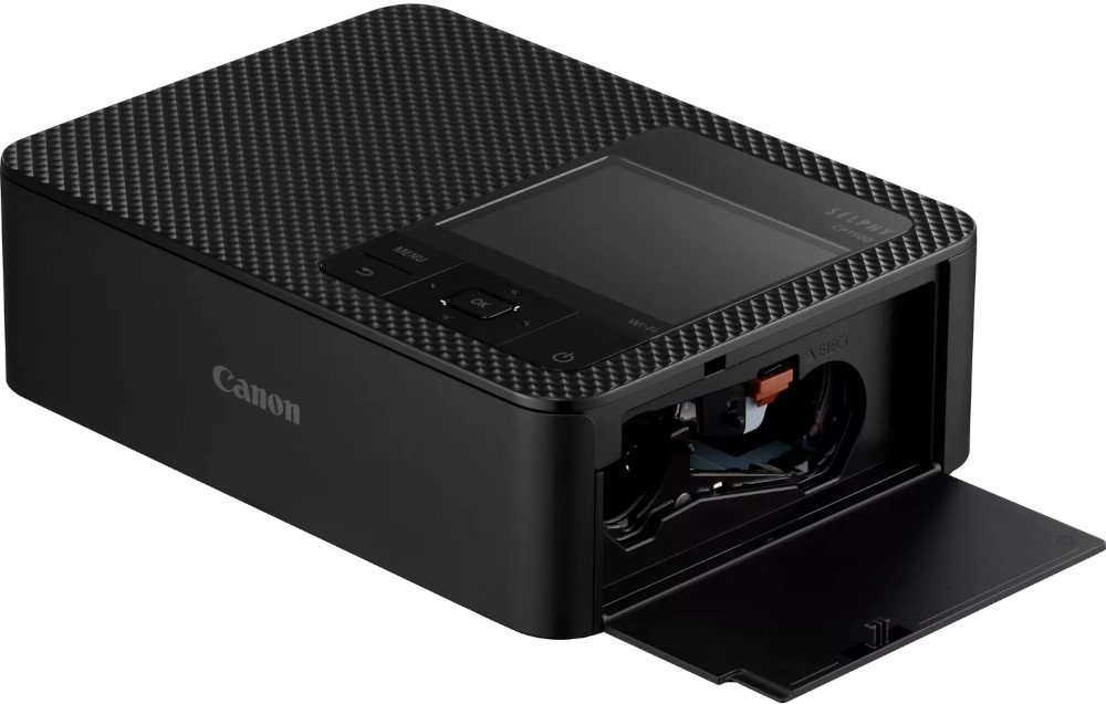 Black Canon Selphy CP1300 printer with open paper tray. Black textured surface.