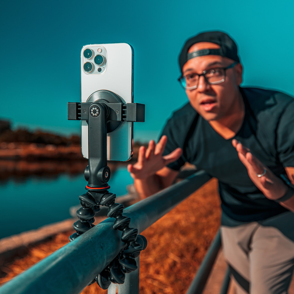 A man recording a video with a phone mounted on a tripod near a lake.