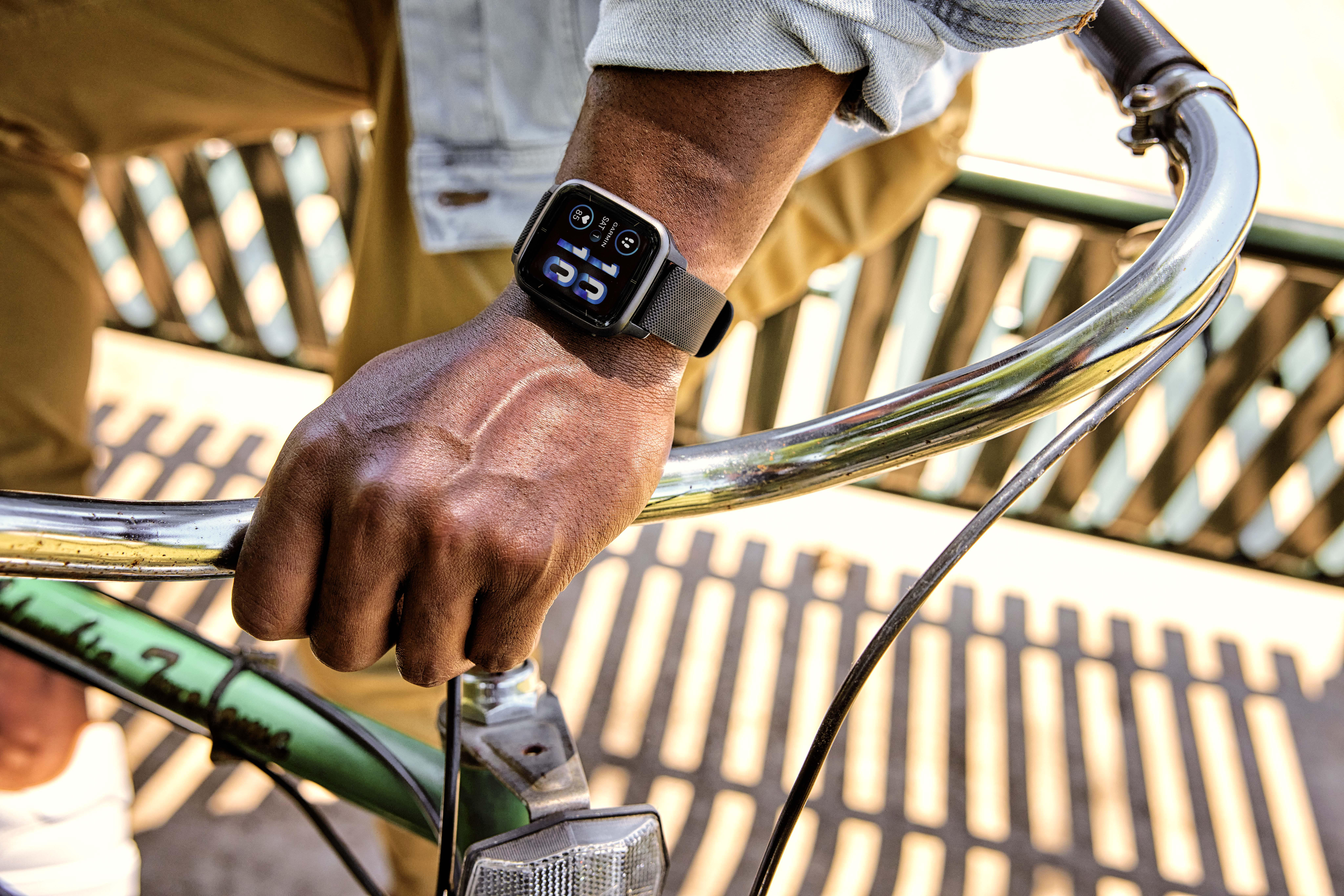 Die Hand einer Person, die einen Fahrradlenker hält, mit einer Smartwatch am Handgelenk, die Daten anzeigt.