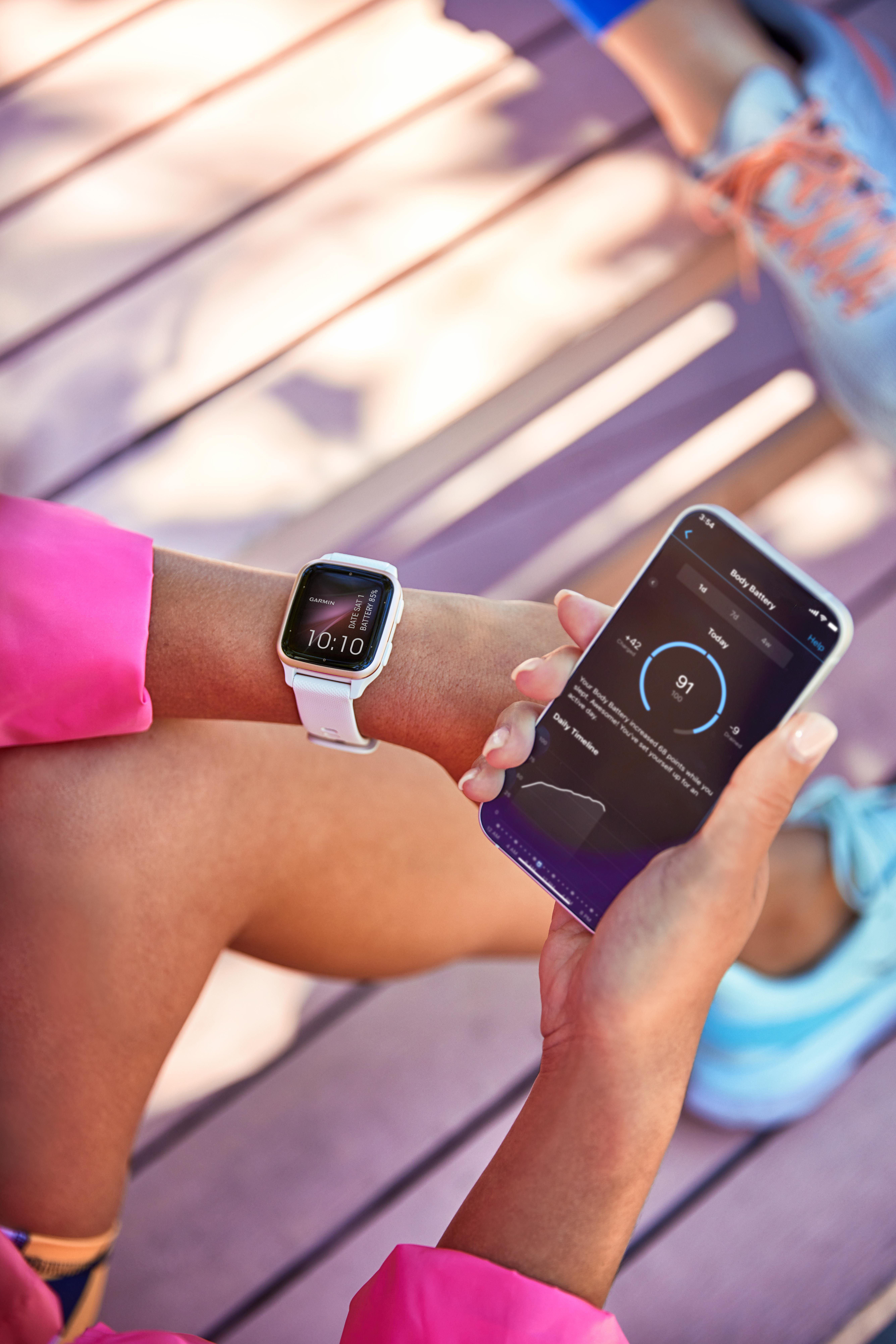 Handgelenk mit Garmin Smartwatch, die Zeit und Akku anzeigt, und Telefon mit Akkuinfo.