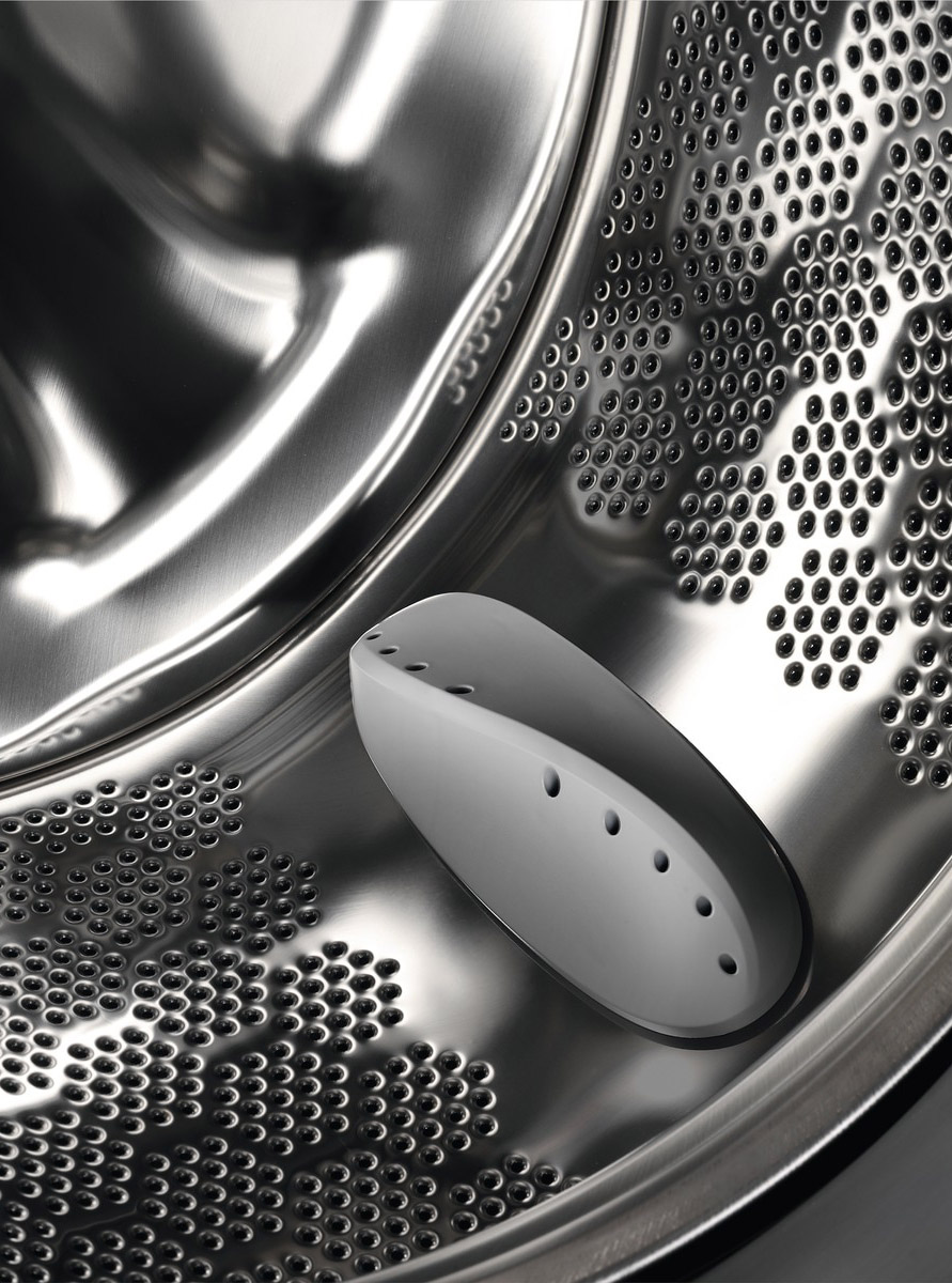 Inside a washing machine drum. A white, perforated plastic piece is on the drum's surface.
