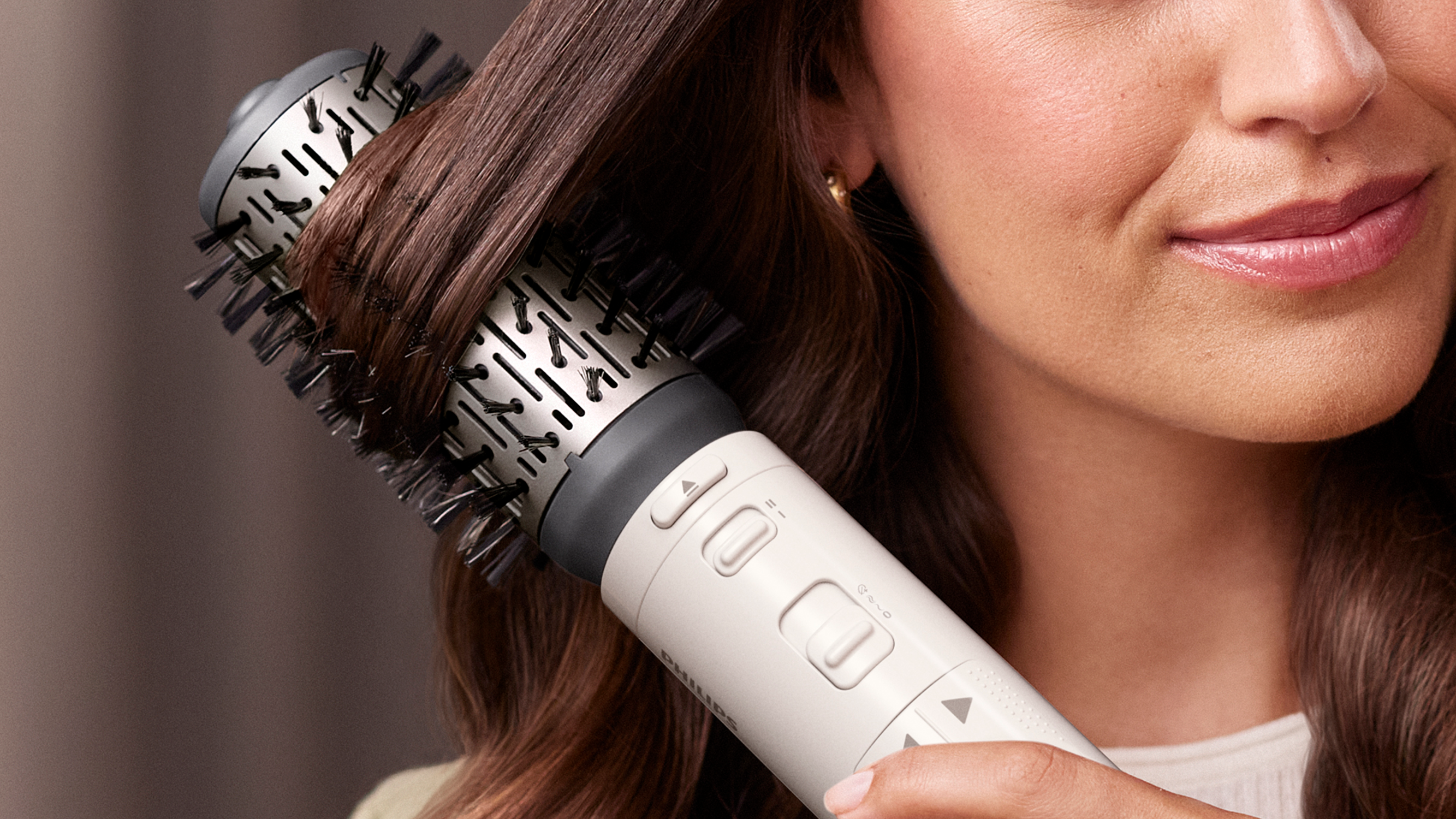 A woman uses a hair styling brush on her brown hair. The brush is white and black.