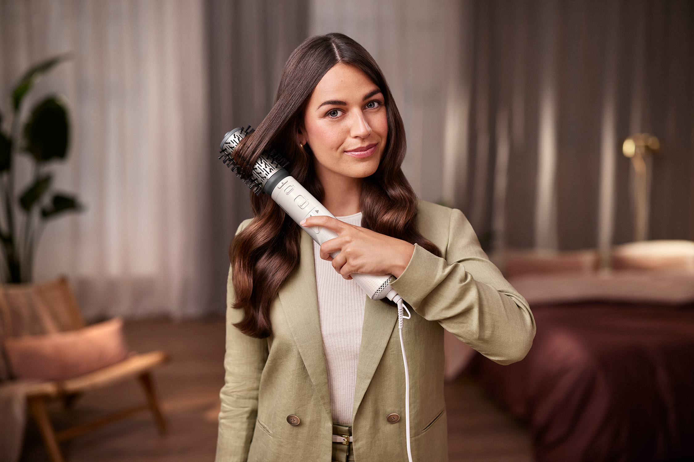 A woman holding a hair styling tool. She is smiling and looking at the camera.