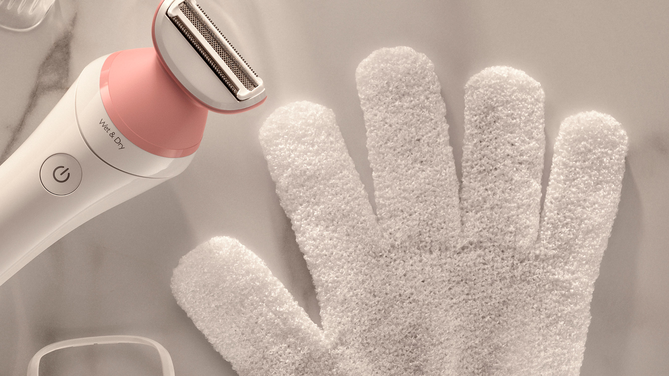 An epilator and a white textured glove rest on a light marble surface.