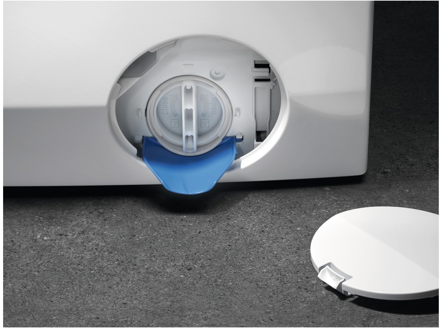 A blue flap reveals a white washing machine filter. A round lid lies nearby.