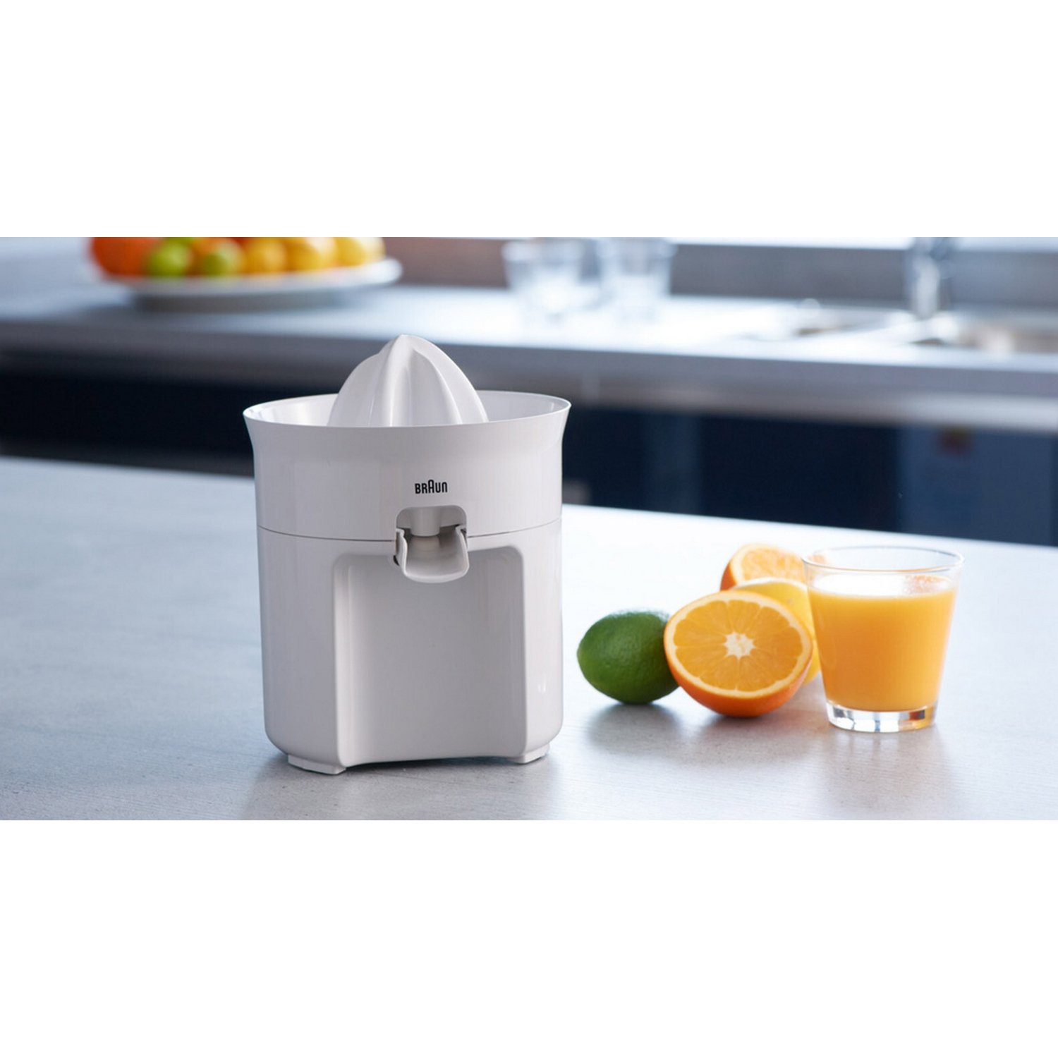 Exprimidor de cítricos Braun blanco con un vaso de zumo, media naranja, lima. Fondo: encimera de cocina.