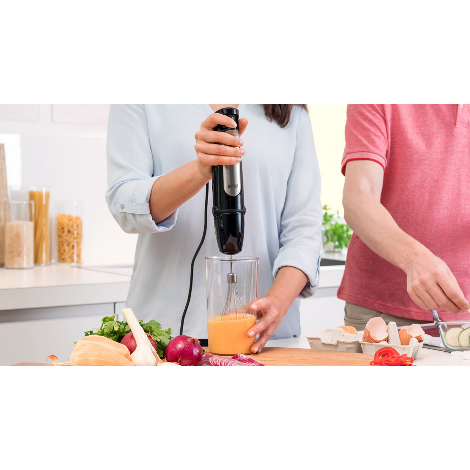 Gente preparando comida. Una persona usa una batidora de mano para mezclar ingredientes en un vaso.