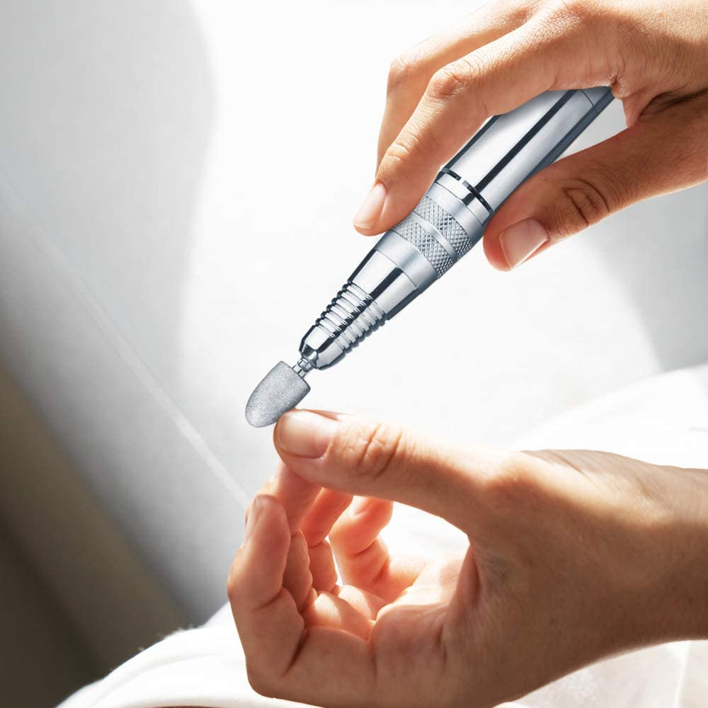 Mains tenant une perceuse à ongles argentée. La perceuse pointe vers un ongle.