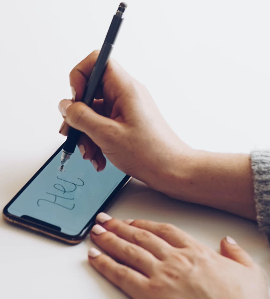 Une main écrivant 'Bonjour' sur l'écran d'un téléphone avec un stylet.