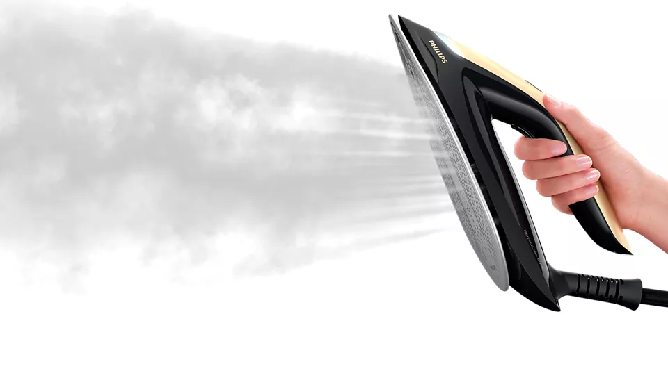 A black and gold iron with steam being released, held by a hand against a white backdrop.