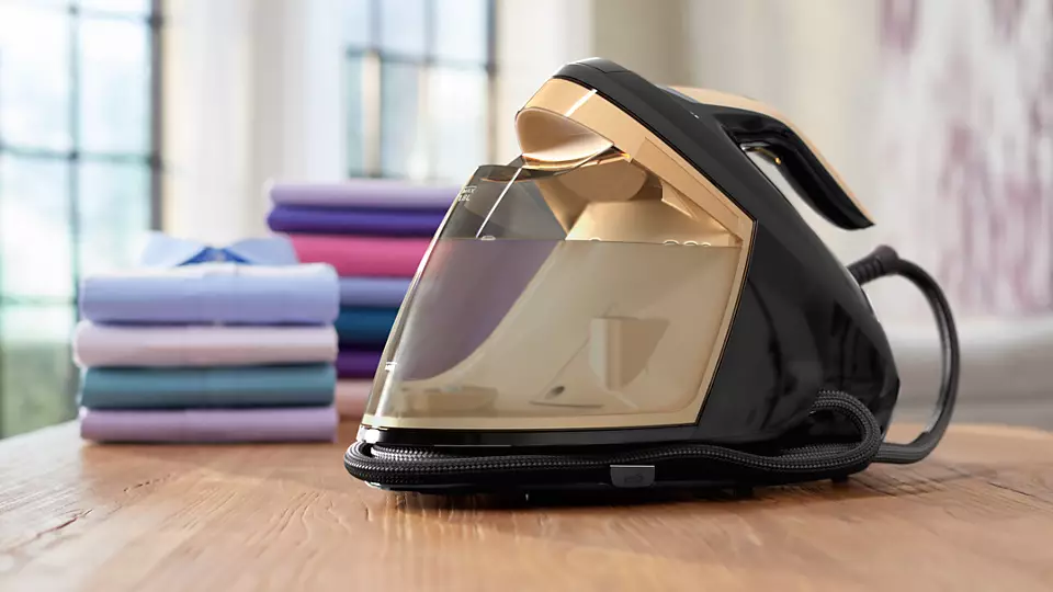 Black and gold steam iron on a wooden table, with folded shirts in the background.