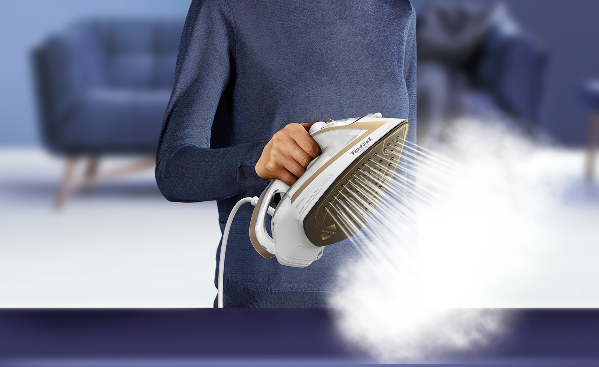 A person ironing clothes with a white and gold iron. Steam is visible.