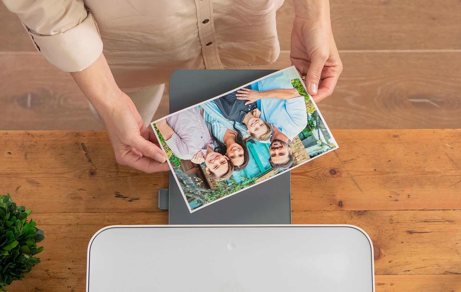 Les mains d'une personne tenant une photo de famille au-dessus d'une imprimante sur une table en bois.
