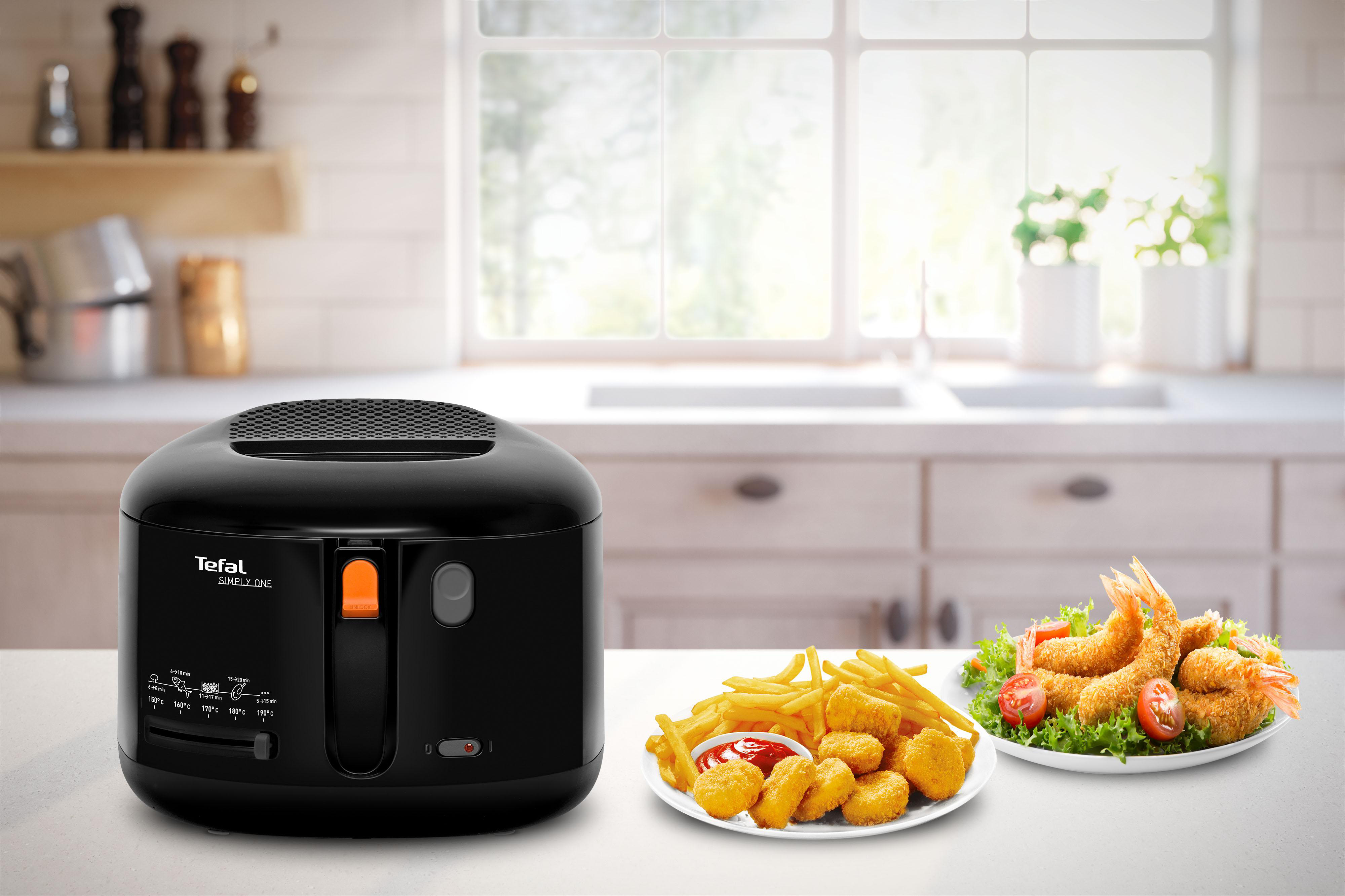 Schwarze Fritteuse mit Pommes, Chicken Nuggets und gebratenen Garnelen auf dem Tisch in der Küche.