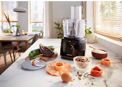 A food processor on a counter. Ingredients and accessories are in front of it.