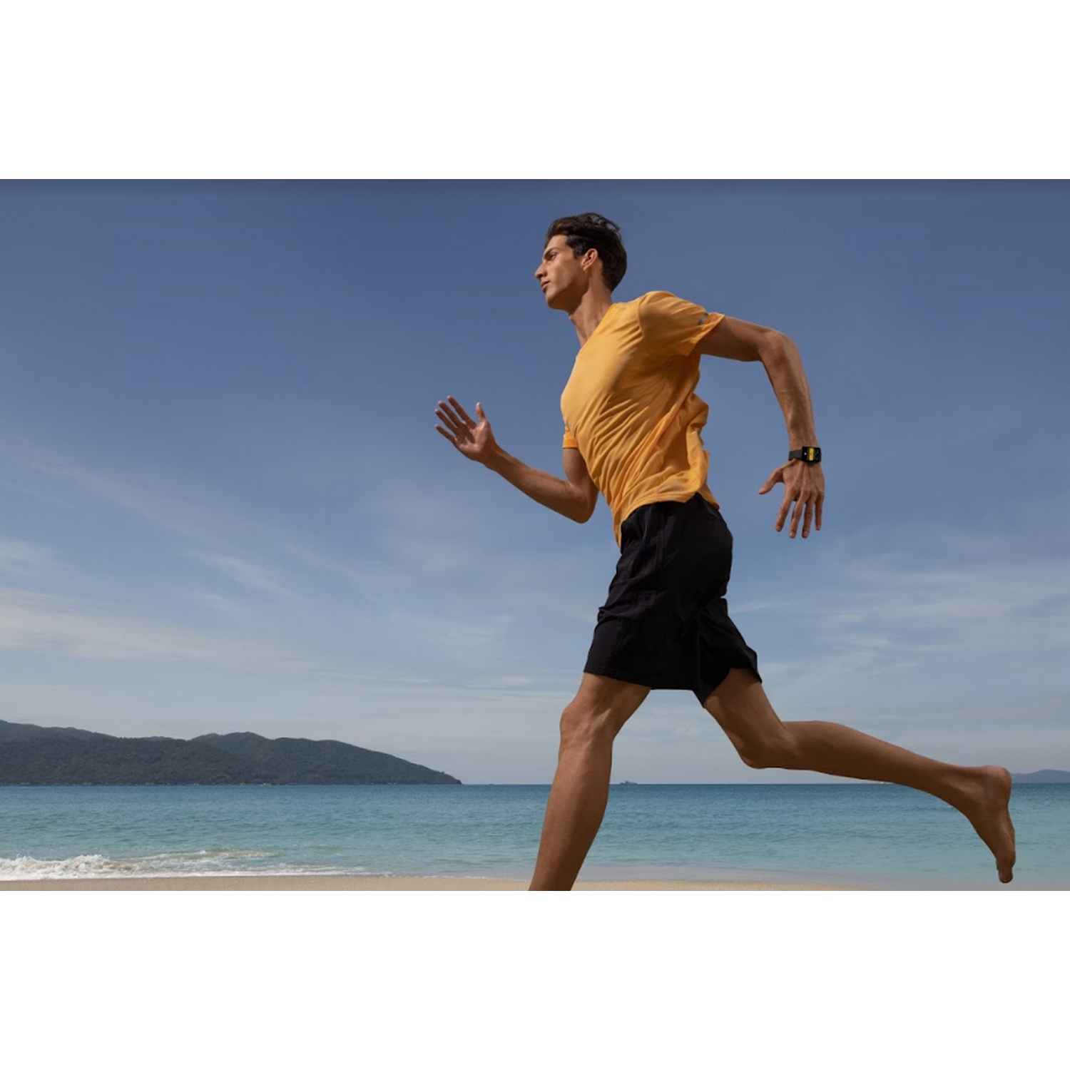 Hombre corriendo en la playa, con camisa amarilla, pantalones cortos y reloj.