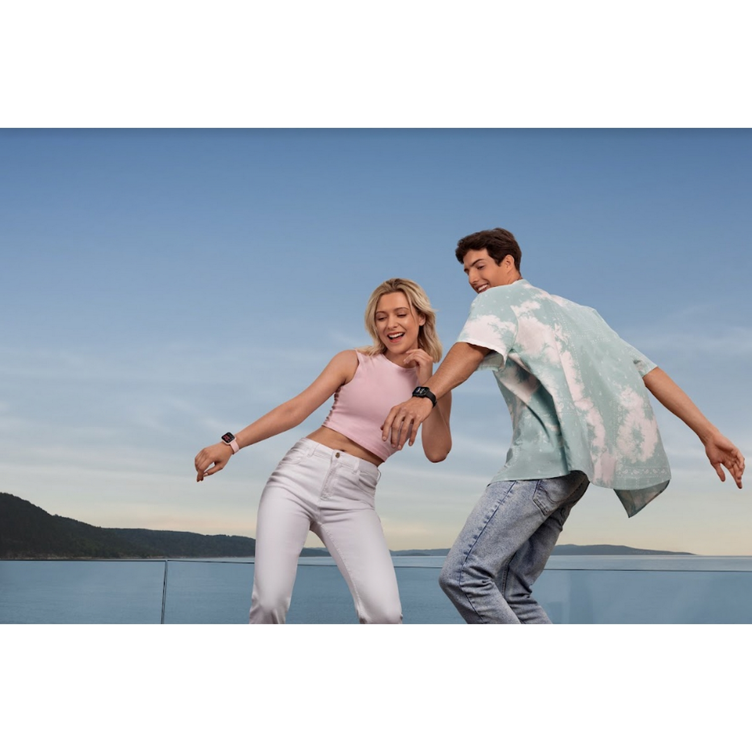 Dos personas bailando al aire libre con smartwatches en sus muñecas, cielo azul.