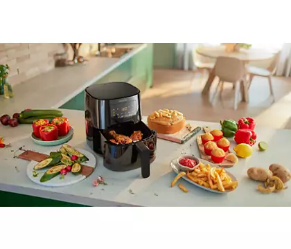 Black air fryer with cooked food, and other dishes with food on a white countertop.