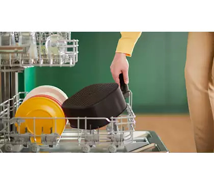 A hand places a black air fryer basket into a dishwasher rack.