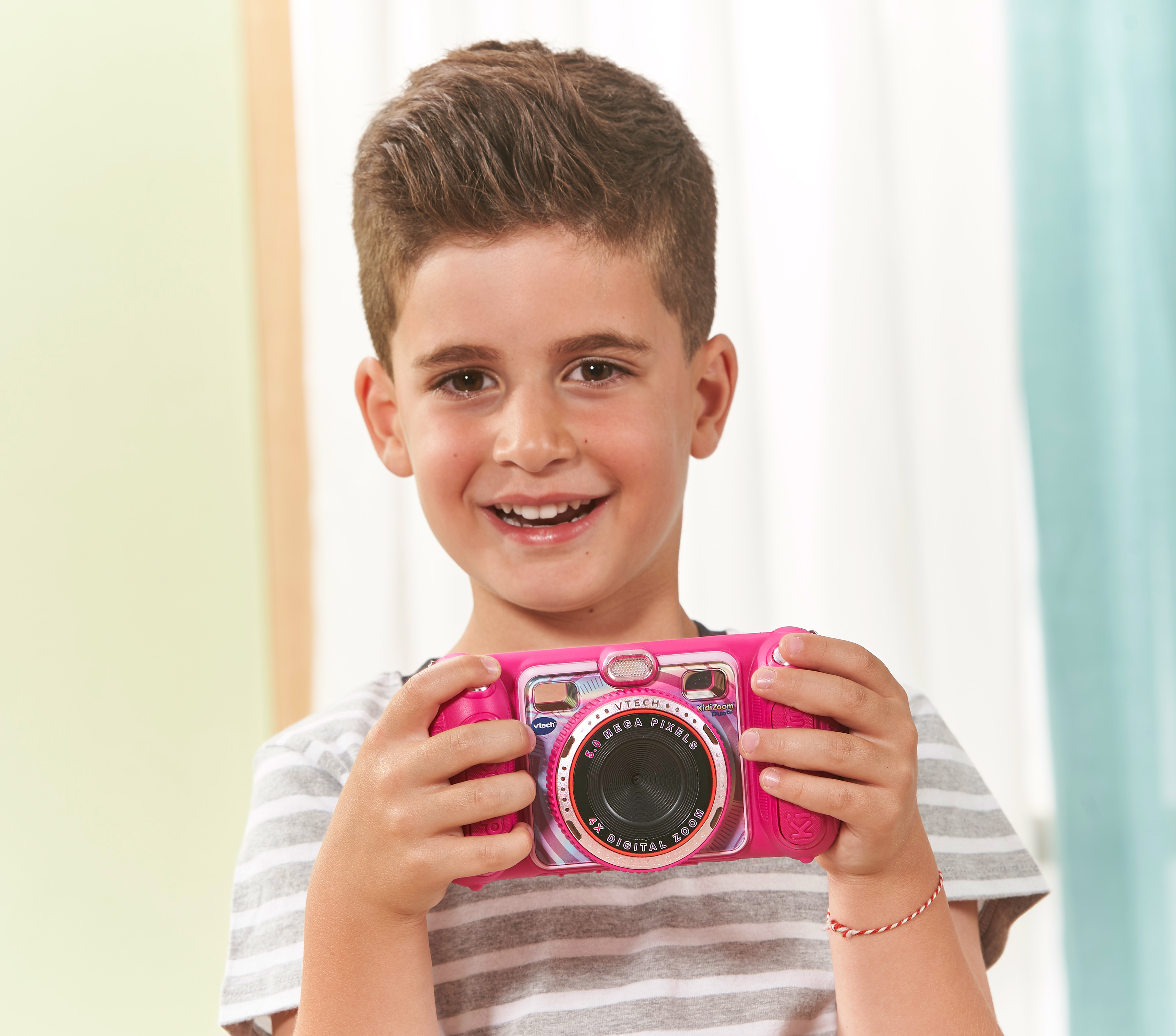Junge hält eine rosa Kinderkamera und lächelt.