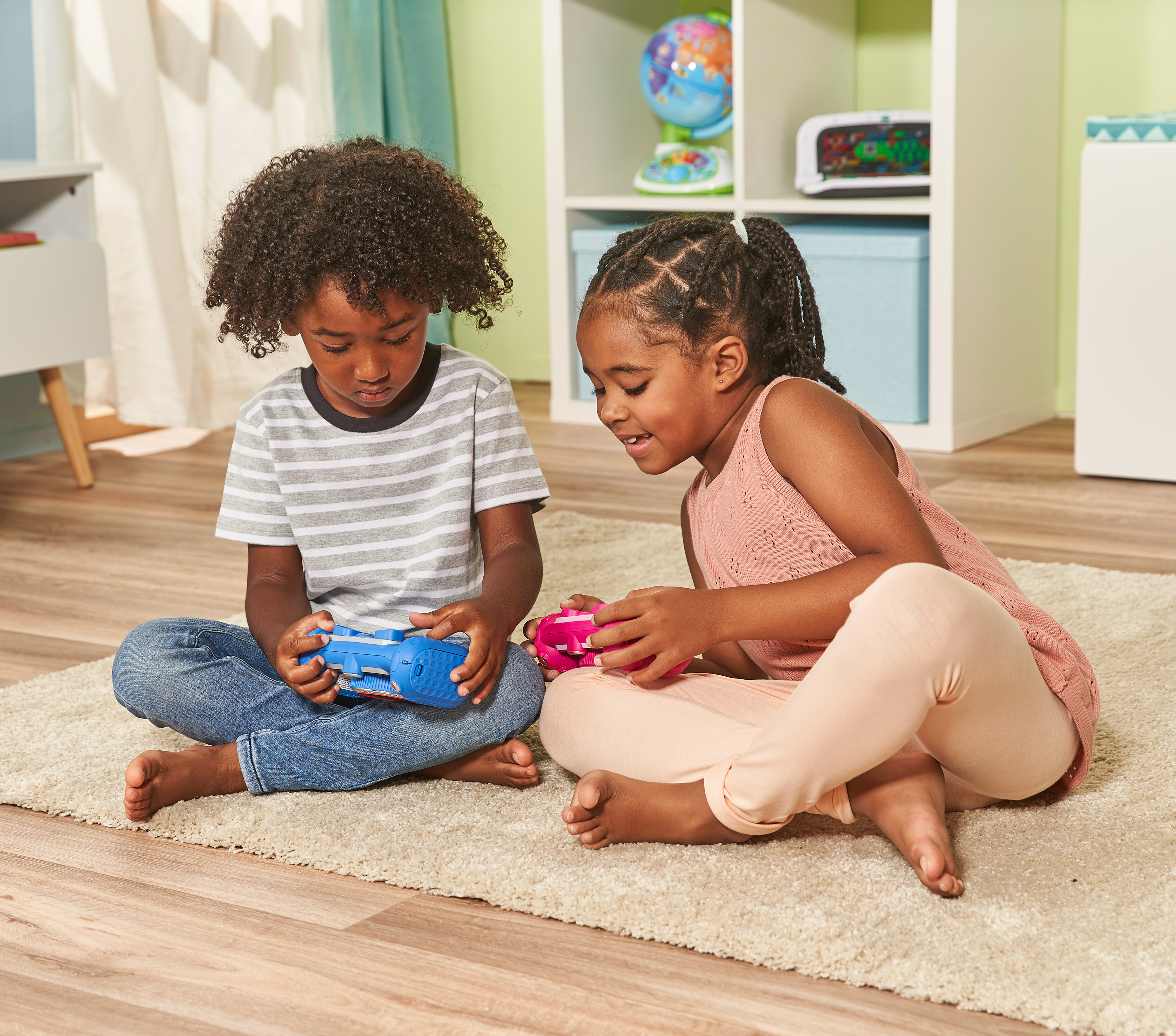 Zwei Kinder spielen auf einem Teppich mit Spielzeugkameras.