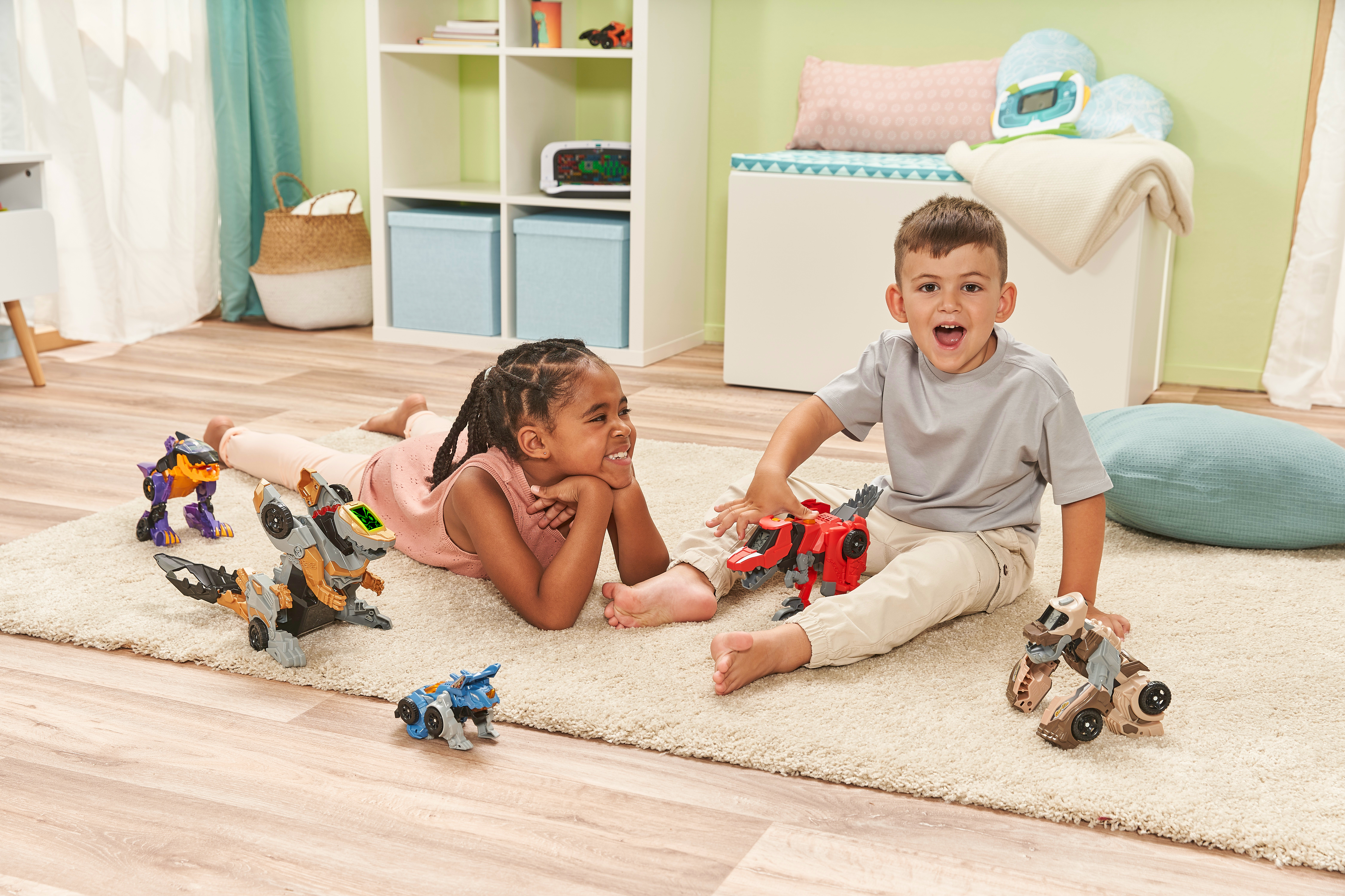 Zwei Kinder spielen auf einem Teppich mit Spielzeugdinosauriern. Spielzeuge sind verschiedenfarbig.