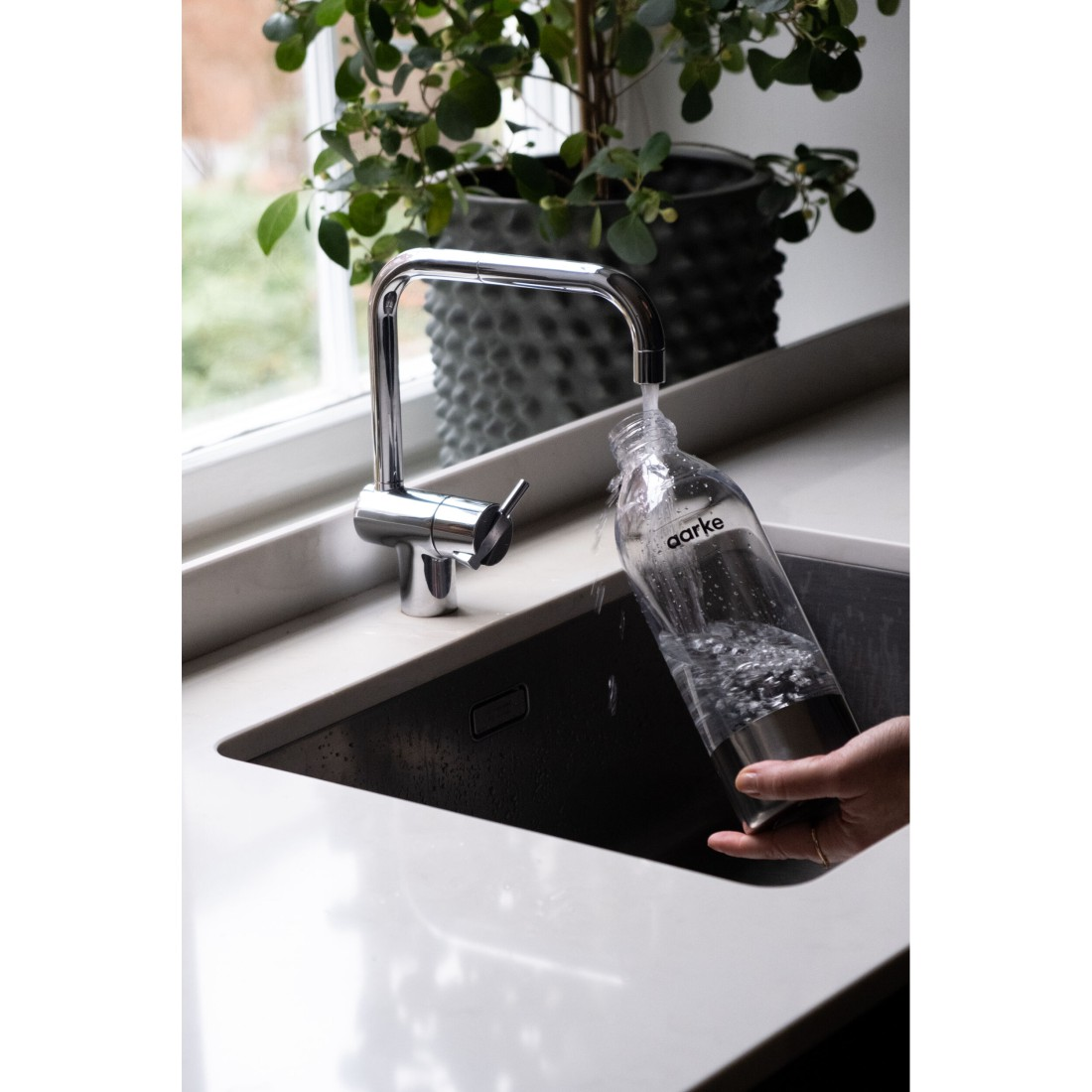 Eine Hand füllt eine Flasche mit Wasser aus einer Chromarmatur.