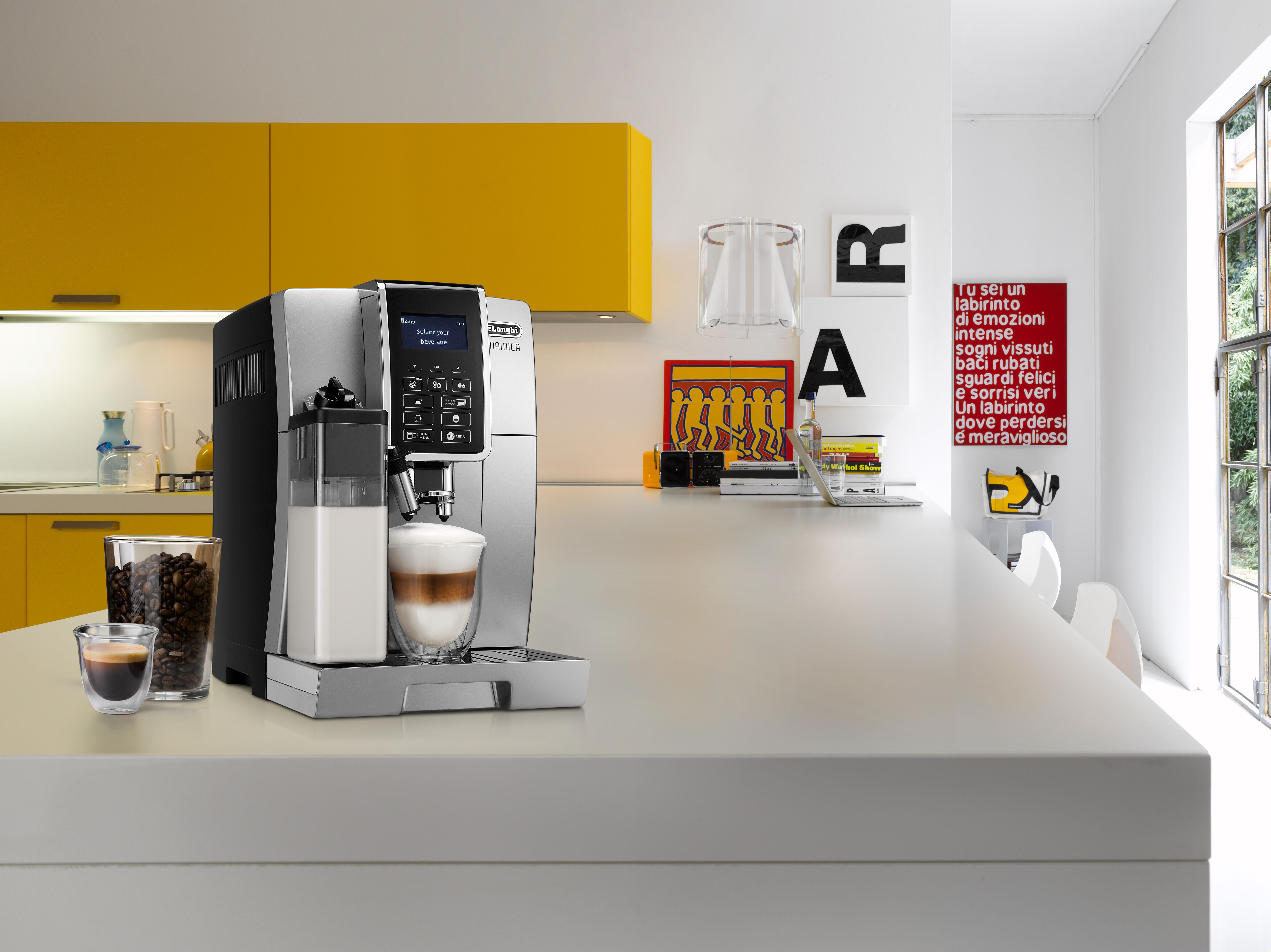Eine silberne und schwarze Espressomaschine mit einem Glas Latte auf einer weißen Theke.