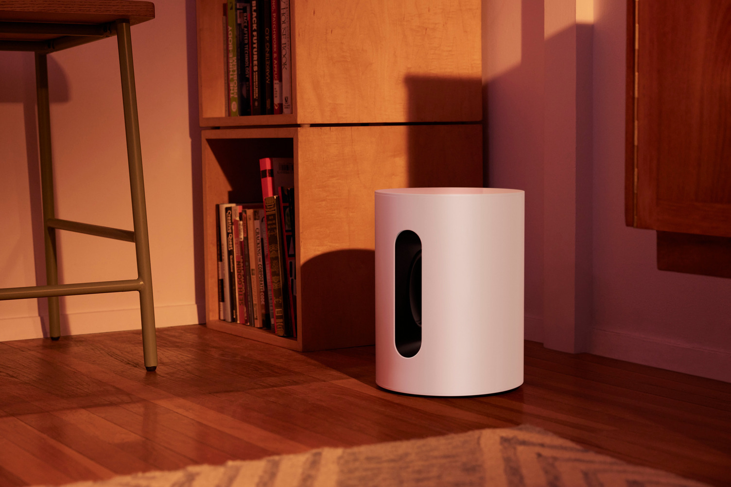 White subwoofer on a wooden floor. There are books and a chair in the background.