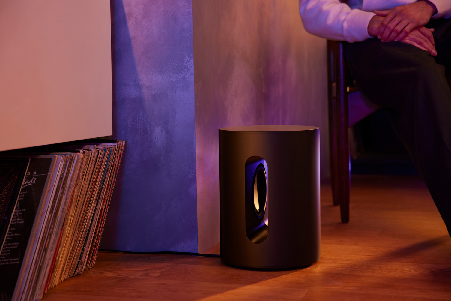 Subwoofer naast een muur en een persoon die op een stoel zit. Het apparaat is rond.