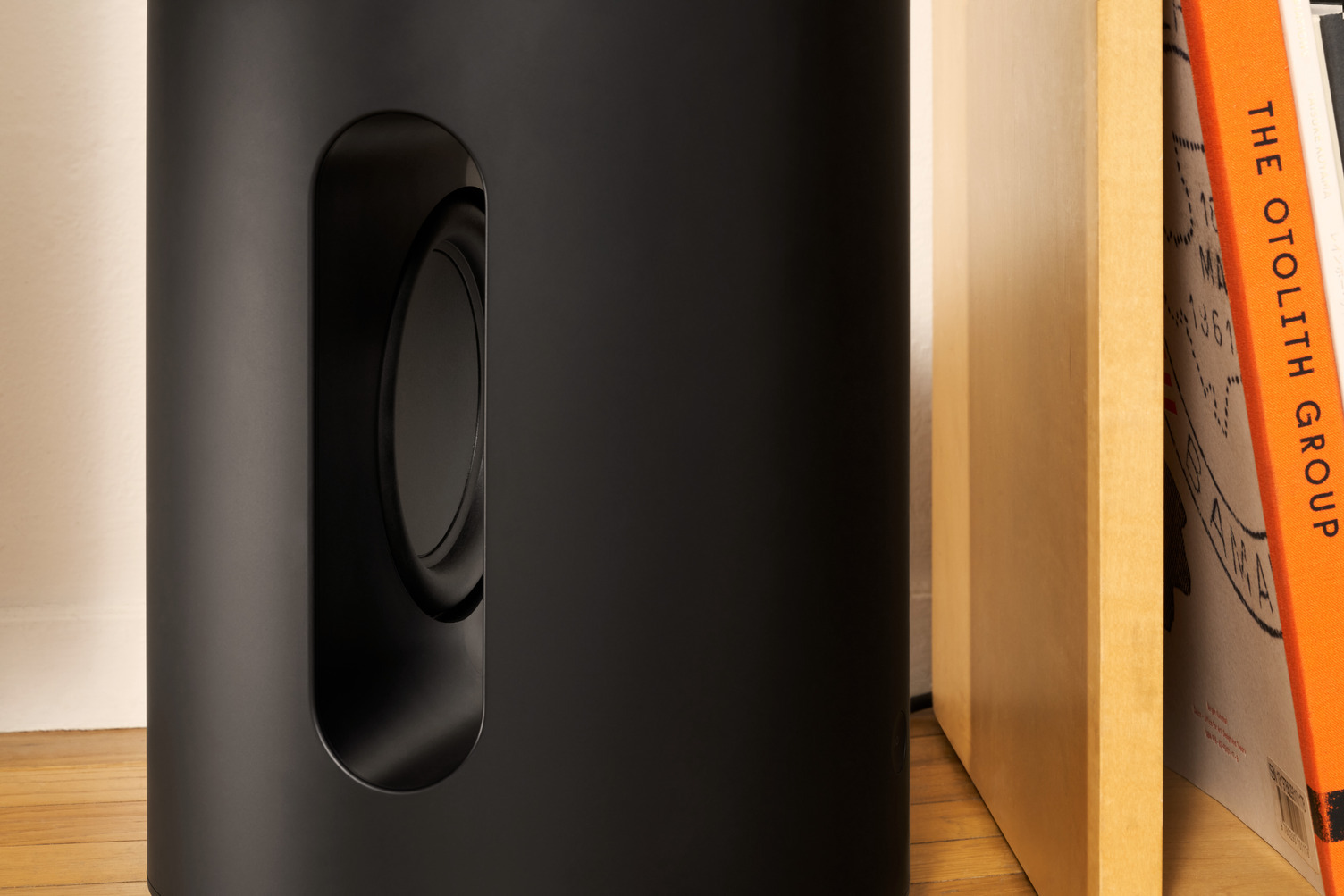 Een zwarte subwoofer naast een boekenplank met boeken. De subwoofer heeft een ronde opening.