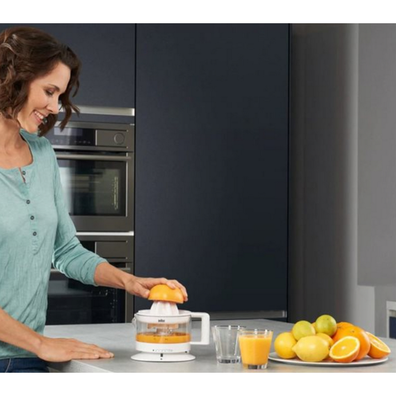 Mujer usando exprimidor de cítricos blanco con naranjas en el mostrador y vasos.