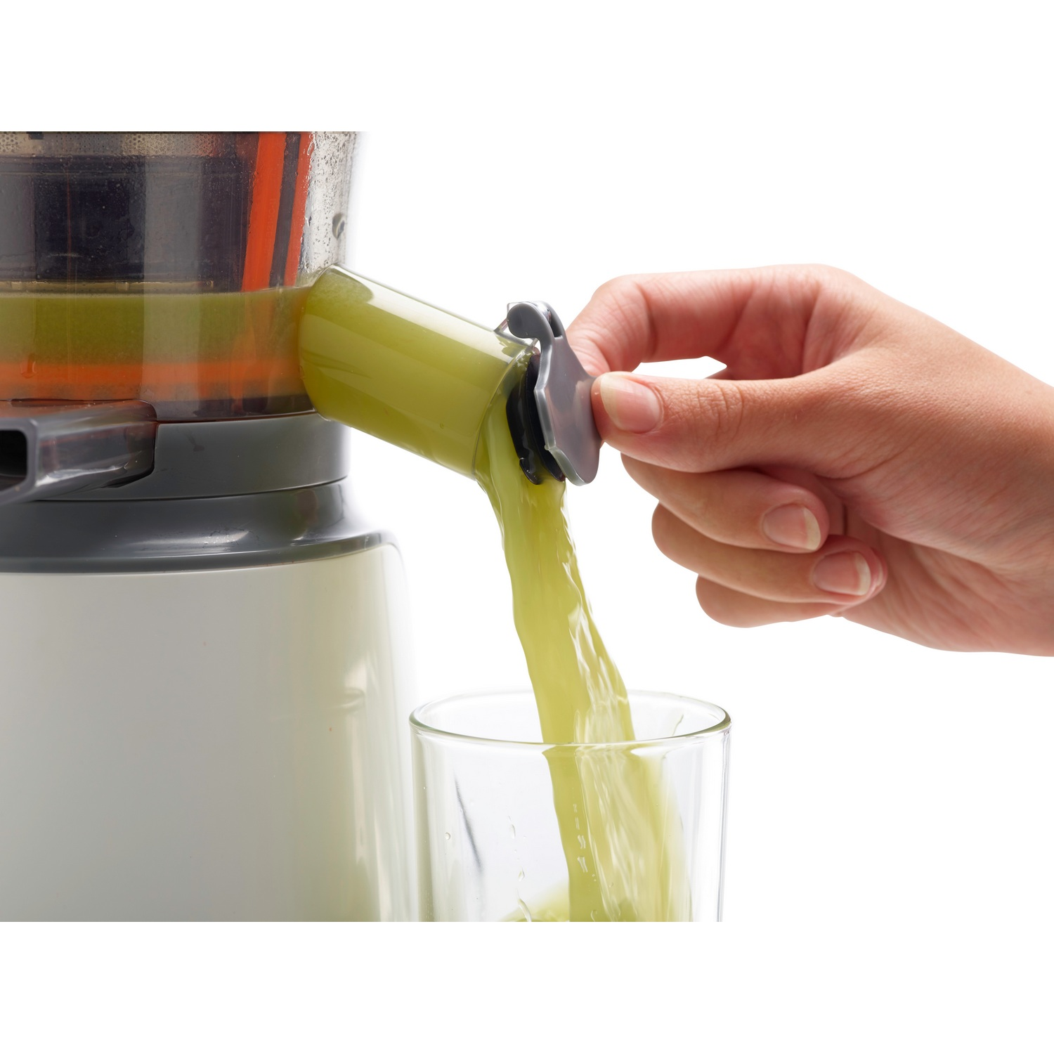 Una persona vierte jugo verde de una exprimidora en un vaso. La exprimidora es blanca y gris.