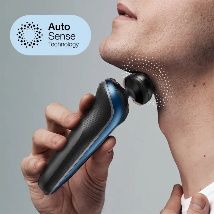 A man shaves his neck with a blue and black electric shaver. The shaver has a black head and a blue handle.