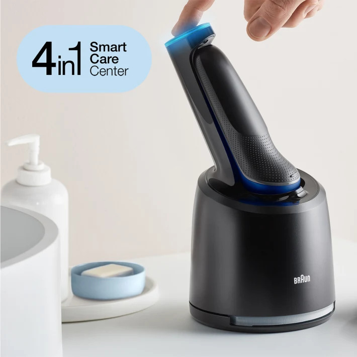 A black shaver with a charging station. A hand is touching the charging station.