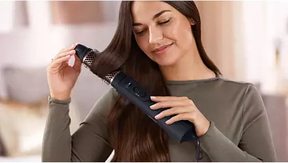 A woman styling her hair with a black and gold hair styler.