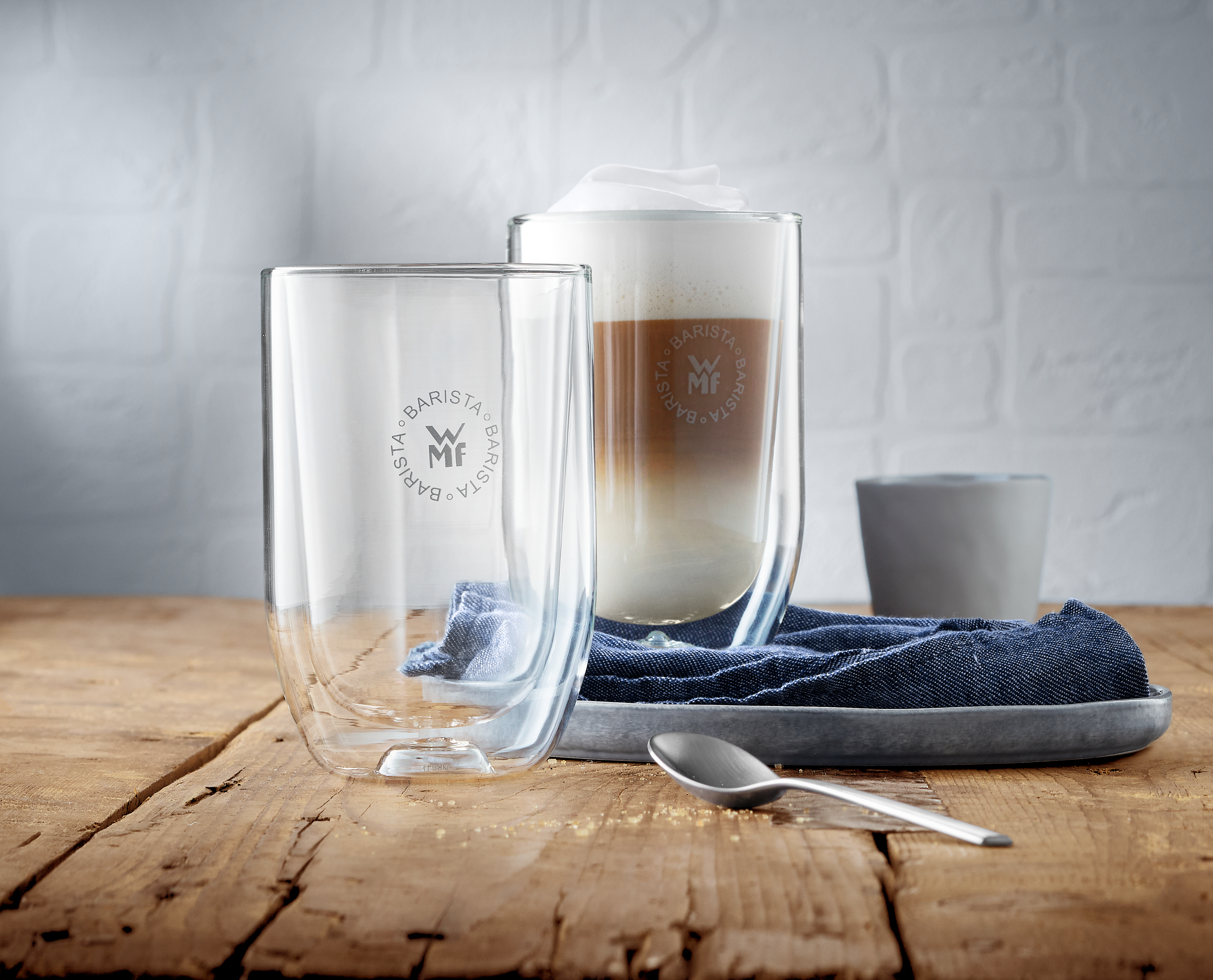 Zwei klare Gläser und ein Latte-Glas mit Schaum. Alle stehen auf einem Holztisch.