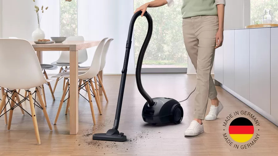 Vrouw die een houten vloer stofzuigt met een zwarte stofzuiger. Made in Germany.