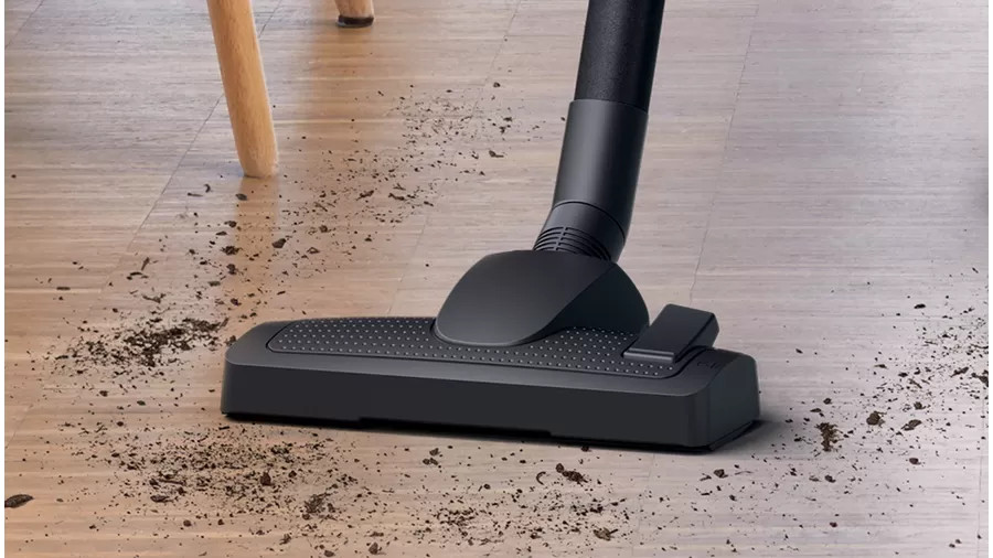 Een zwarte stofzuigerkop op een houten vloer, die vuil opzuigt.