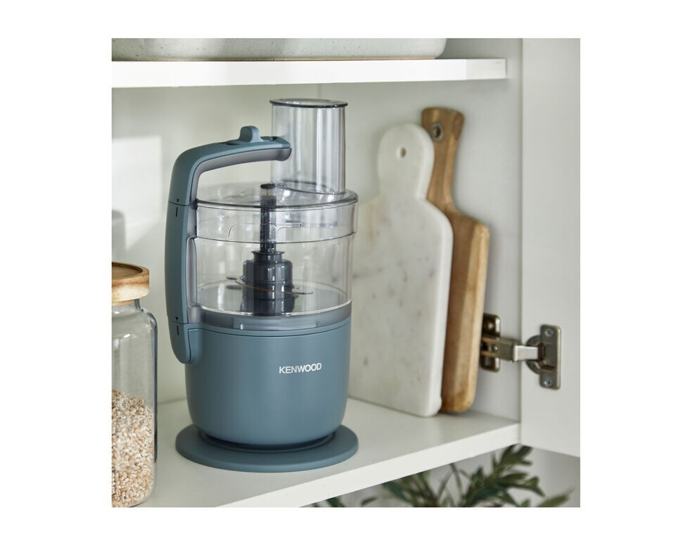 A food processor in a white cabinet. There are cutting boards and jars.