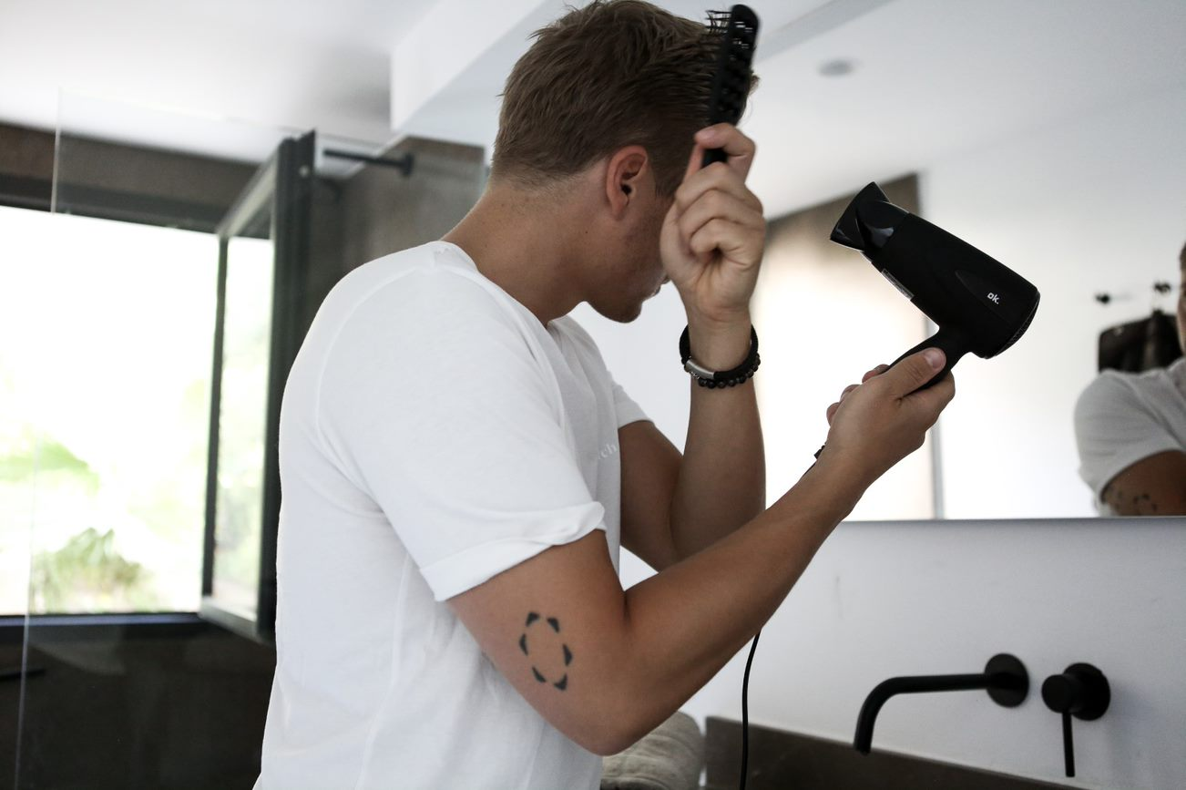 A man using a hair dryer in a bathroom, looking into a mirror.